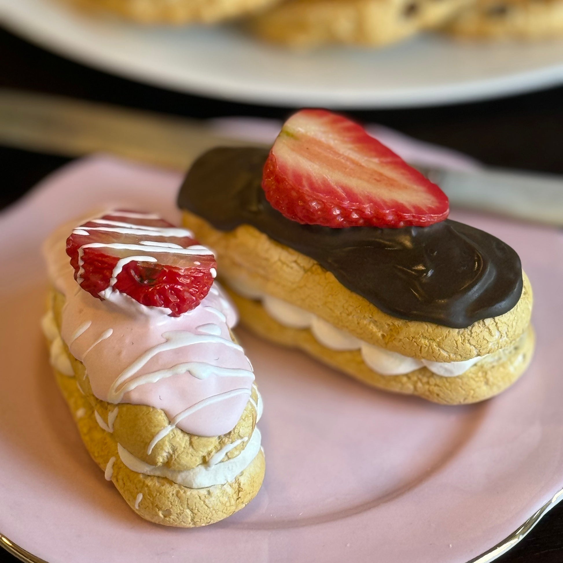 Two replica pastries with strawberry toppings on a pink plate, with cookies in the background.