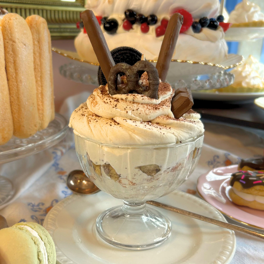Dessert with whipped cream and cookies on a table with macarons and other treats.