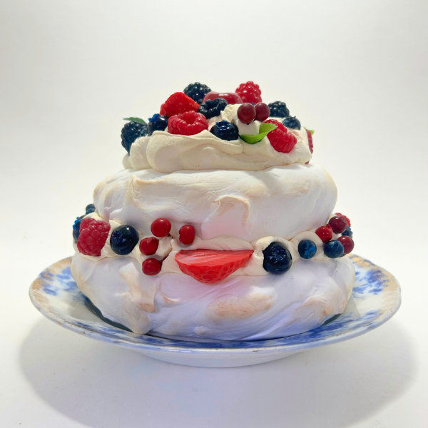 Two-layered meringue dessert with fresh berries on a decorative plate against a white background