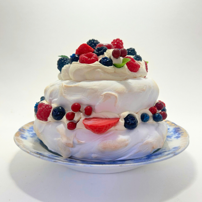 Two-layered meringue dessert with fresh berries on a decorative plate against a white background